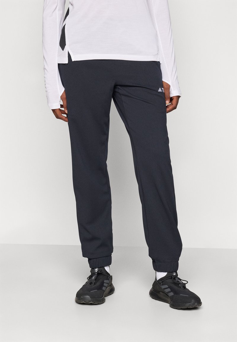 Schwarze Sporthose mit elastischem Bund, Bündchen am Knöchel und dezentem Logo-Detail am Bein, kombiniert mit dunklen Laufschuhen und weißen Socken.