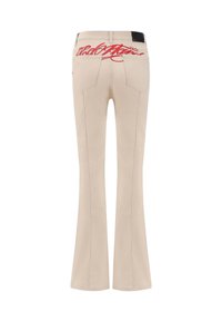 Beige utsvängda jeans med röd broderad logotyp på baksidan, med standardfickor och kontrasterande sömnad. Slät tygstruktur.