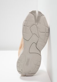 Semelle de basket Puma, avec une tige beige clair, une semelle extérieure en caoutchouc texturée avec des rainures, et une semelle intermédiaire grise. Logo de la marque sur le côté.