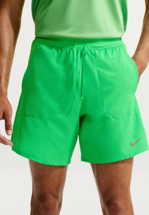 Homme portant un short de sport vert vif avec une ceinture élastique et un cordon, avec un petit logo Nike sur la jambe gauche.