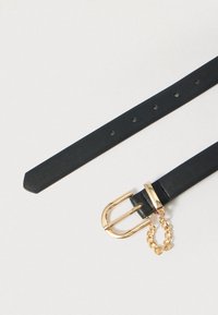 Μαύρη δερμάτινη ζώνη με αγκράφα διπλής καρφίτσας σε χρυσό τόνο και διακόσμηση αλυσίδας, χαρακτηριζόμενη από ομοιόμορφα κατανεμημένες τρύπες και κωνικό άκρο.