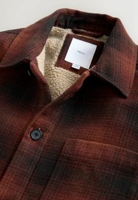 Flanellhemd in rot-schwarzem Karomuster mit einem mit Sherpa gefütterten Kragen. Verfügt über eine Brusttasche und ein schwarzes Knopfdetail. Markenlabel sichtbar.
