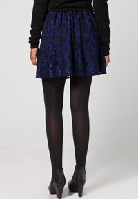 Gonna da pattinatrice in pizzo nera con motivo floreale blu, caratterizzata da una vita arricciata. Indossata con collant neri e stivaletti alla caviglia.