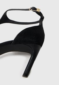 Melni augstpapēžu sūkņi ar elegantu dizainu, kas iekļauj teksturētu augšējo materiālu, potītes siksniņu un zelta toņa akcentus.
