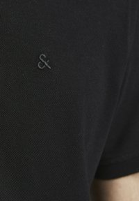 Zwart katoenen polo shirt met een gemêleerde stof, korte mouwen en een klein, verhoogd logo op het linker borstgedeelte.