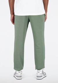 Zelené tepláky z měkké látky, s volným střihem, elastickými manžetami a bočními kapsami. Kombinované s šedými a bílými teniskami.