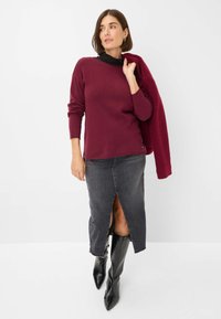 Maglione bordeaux a maniche lunghe abbinato a una gonna di jeans grigia con uno spacco anteriore, completato da stivali neri alti a punta.