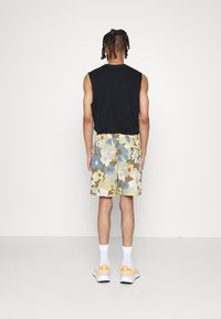 Canotta nera senza maniche e pantaloni corti con motivo floreale nei colori beige, blu e verde. Calzini bianchi e sneaker con accenti arancioni completano l'outfit.