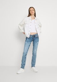 Vit denimjacka med knäppning och fickor, ihop med ljusblå slitna jeans och vita sneakers. Enkel, avslappnad outfit.