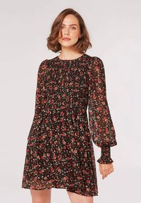 Schwarzes Blumenkleid mit langen, gepufften Ärmeln, einem gerafften Oberteil und einem schwingenden Rock. Der Stoff hat eine durchscheinende Textur mit kleinen roten und grünen Blumen.