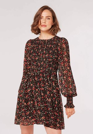 Schwarzes Blumenkleid mit langen, gepufften Ärmeln, einem gerafften Oberteil und einem schwingenden Rock. Der Stoff hat eine durchscheinende Textur mit kleinen roten und grünen Blumen.