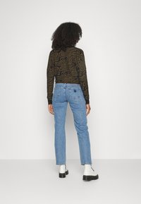 Maglietta a maniche lunghe nera e marrone a fantasia abbinata a jeans dritti blu chiaro e stivali platform neri, vista da dietro.