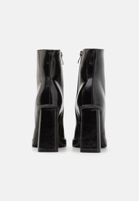 Cizme din piele neagră până la gleznă cu toc bloc înalt, fermoare laterale și textură netedă, lucioasă. Linii curate și design minimalist.