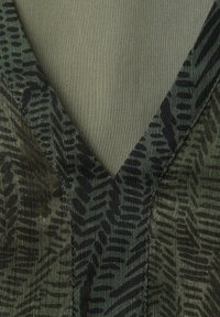 Gros plan sur un chemisier à col en V avec un motif abstrait en zigzag noir et vert foncé sur un tissu texturé.