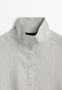 Chemise gris clair rayée verticalement avec un col montant et quatre boutons couleur crème sur le devant.
