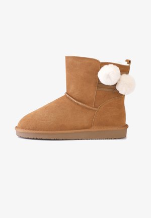 Beige Wildleder-Stiefeletten mit runder Spitze, weicher Innenausstattung und zwei weißen Pompons an der Seite. Strukturierte Gummisohle.