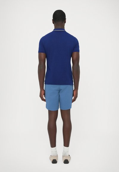 Tengerészkék rövid ujjú galléros póló, világoskék rövidnadrág párosításával. Puha anyag, testhez álló fazon, egyszínű textúra és minimális részletezés.