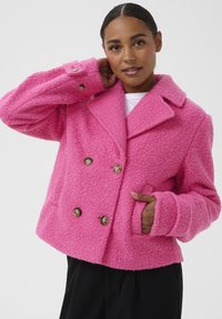 Veste double boutonnage rose vif en tissu texturé, avec un col, de grands boutons et des poches latérales. Coupe décontractée avec des manches surdimensionnées.
