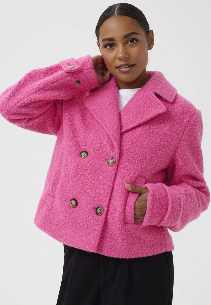 Veste double boutonnage rose vif en tissu texturé, avec un col, de grands boutons et des poches latérales. Coupe décontractée avec des manches surdimensionnées.