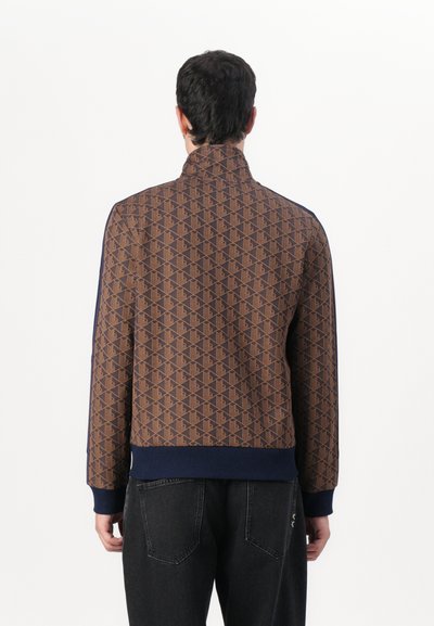 Veste marron à motif avec col montant, accents navy, poignets et ourlet côtelés. Texture lisse avec des motifs géométriques tout au long.