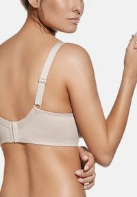 Sostén beige con tirantes ajustables, textura suave y cierre de gancho y ojal. Diseño simple sin patrones visibles ni adornos.