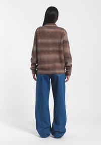 Maglione a righe marroni realizzato in morbido materiale peloso, abbinato a pantaloni in denim blu larghi. Polsini e colletto del maglione visibili, vestibilità rilassata.