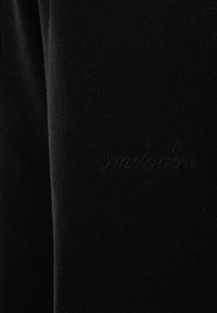 Zwarte stof met subtiele, ingestikte tekst "smilodone" die opgaat in het materiaal, met zichtbare textuur en details van de stof.