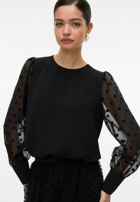 Must mustre, millel on tekstureeritud keha ja läbipaistvad, täpilised puffvarrukad, ümmargune kaelus ja kinnitatud mansetid randme kohal.