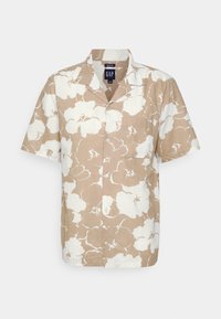 Camicia a maniche corte in beige con motivo floreale bianco, realizzata in un tessuto leggero, con colletto a punte e tasca frontale.