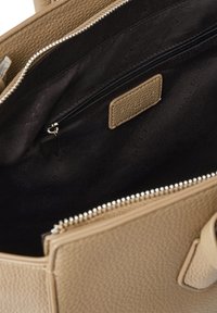 Interno di una borsa a tracolla in pelle beige con fodera nera, dotata di una tasca con zip, texture liscia e dettagli metallici della zip.