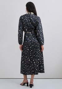 Vestido largo negro con estampado de leopardo, con mangas largas, un cinturón en la cintura y un cuello en contraste. Tela suave y diseño hasta los tobillos.