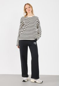 Pasiasty czarno-kremowy longsleeve połączony z czarnymi dresami z nadrukiem "TOKIO 1959", uzupełniony szaro-czarnymi trampkami.