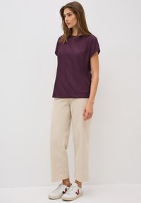 Purple textured short-sleeve top with a zigzag pattern paired with light beige cropped pants and white sneakers featuring maroon accents.