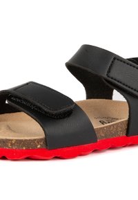 Sandales noires avec deux sangles velcro. Semelle en liège avec une texture lisse. Semelle extérieure en caoutchouc rouge vif avec un motif de traction texturé.