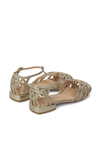 Sandalias planas doradas con tiras, que presentan un intrincado diseño de rejilla y una superficie metálica brillante. Con punta abierta y detalle de correa en el tobillo.