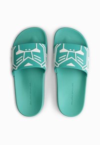 Turquoise slide sandals with a textured footbed. A broad strap features white geometric patterns and branding on the side.