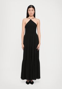 Svart maxikjole med et tettsittende smocket bodice, halterneck og flytende, tiered skjørt. Har gjennomsiktig stoff og en jevn tekstur.