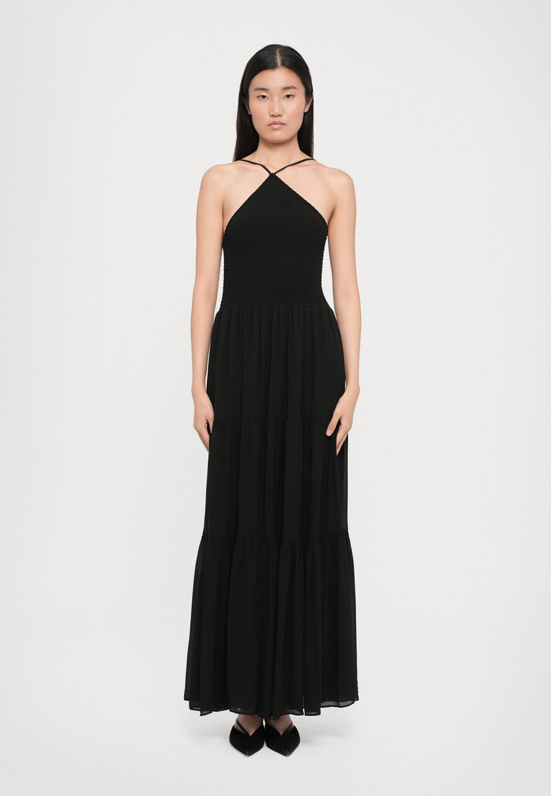 Svart maxikjole med et tettsittende smocket bodice, halterneck og flytende, tiered skjørt. Har gjennomsiktig stoff og en jevn tekstur.