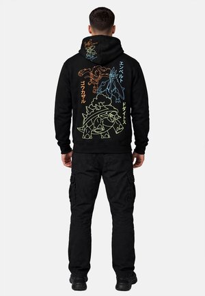 Man die een zwarte hoodie draagt met kleurrijke omrande ontwerpen van drie fictieve wezens en verticale Japanse tekst op de rug.