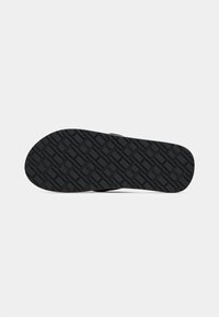 Sole of black flip-flop sandal showing geometric tread pattern with diamond and rectangular shapes on plain background.