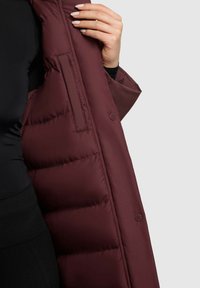 Bordowa kurtka puchowa z gładką, błyszczącą powierzchnią. Posiada boczną kieszeń, pikowane wzornictwo oraz zapięcie na guziki wzdłuż wewnętrznego szwu.