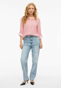 Chemise à rayures rouges et blanches à manches retroussées, associée à un jean décontracté bleu clair et des escarpins noirs à bout pointu.