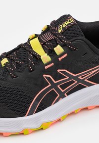 Scarpa da corsa nera con tomaia testurizzata, dettagli in rosa e giallo e un'intersuola bianca. Presenta un design in rete e una suola vivace.