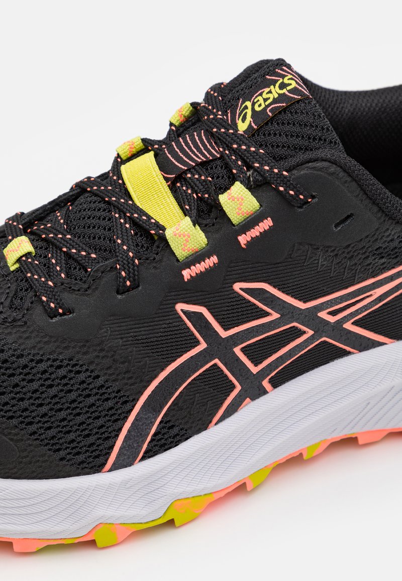 Zapatilla de running negra con parte superior texturizada, acentos en rosa y amarillo, y una entresuela blanca. Presenta un diseño de malla y una suela vibrante.