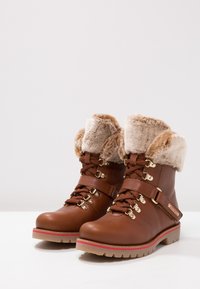 Bruna läderankelstövlar med imitationspäls, metalldetaljer och snörning. Har en texturerad ovandel och en sula med röda detaljer.