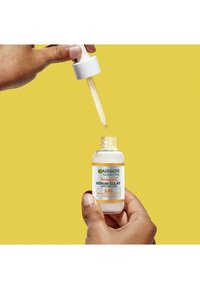 Sérum Vitamin C Garnier SkinActive dans un flacon en verre transparent avec un capuchon compte-gouttes blanc, présentant un liquide jaune clair. L'étiquette affiche du texte en plusieurs langues.