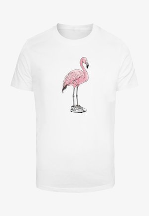 Valge puuvillane t-särk, millel on roosa flamingo graafika, kes kannab spordijalatseid. Kujundus sisaldab detailseid sulgi ja musta nokka.
