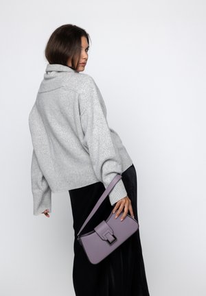 Maglione grigio oversized a maglia con colletto arrotolato, abbinato a una borsa a tracolla in pelle viola con una chiusura metallica quadrata. Gonna nera fluida.