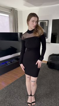 Musta ribbineulottu minimekko, jossa pitkät hihat ja läpinäkyvä verkkokaulus, koristeltu paljetein. Varustettu mustilla remmikkäillä korkokengillä ja näkyvillä jalan tatuoinneilla.