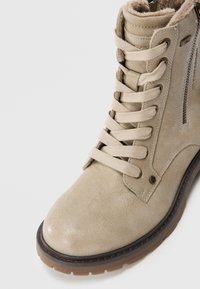 Stivale in pelle beige con lacci, foderato in pelliccia, con zip laterale e suola in gomma marrone, mostrato da un'angolazione ravvicinata su uno sfondo bianco.